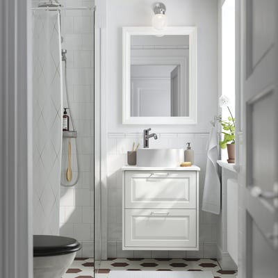 Modernt vitt badrum: hex klinkergolv, handfat i marmor, hängande handdukar, dusch i glas, spegel, enkel glödlampa.