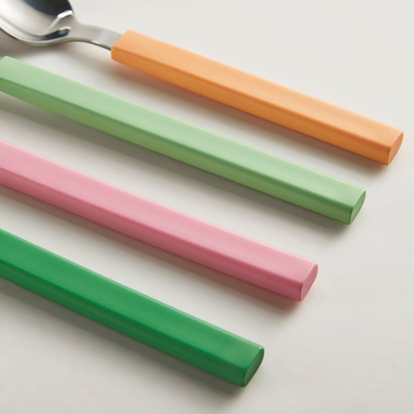 Färgglada bestickuppsättning: orange, gröna, rosa handtag, snyggt ordnade på vit yta.