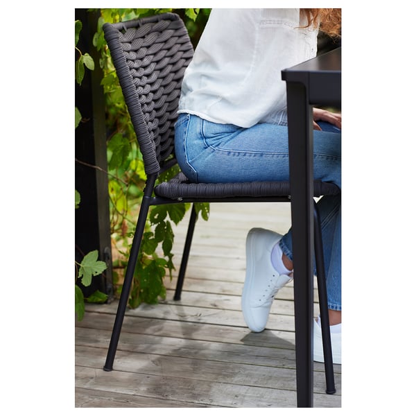 En person som sitter på en grå utomhusstol på TEGELÖN på ett trädäck, klädd i jeans och vita gymnastikskor.