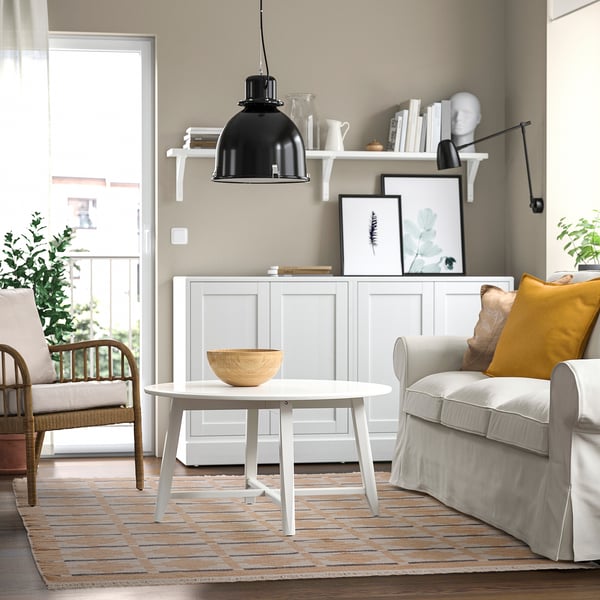 Modernt vardagsrum med grå soffa, matta, trästol och soffbord med skål. Bokhyllan rymmer konst och lampa.