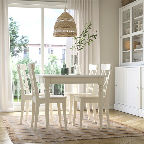 Modern matplats med vit TELEGRAFLINJE-matta, träbord, stolar, hängande lampa och vitrinskåp.