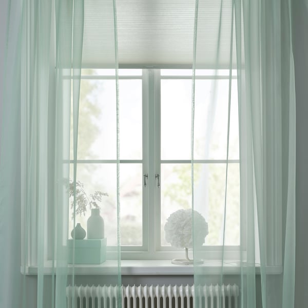 Gröna gardiner på fönster med ren design, mjukt ljus, avskildhet. Radiator nedan, inredning på tröskeln, mysigt rum.