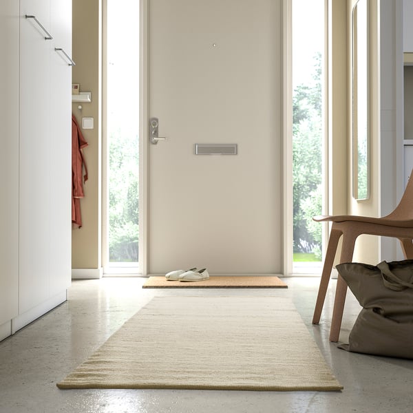 Minimalistisk hall med beige matta i mitten, något större än dörrmattan, mjuk och inbjudande.