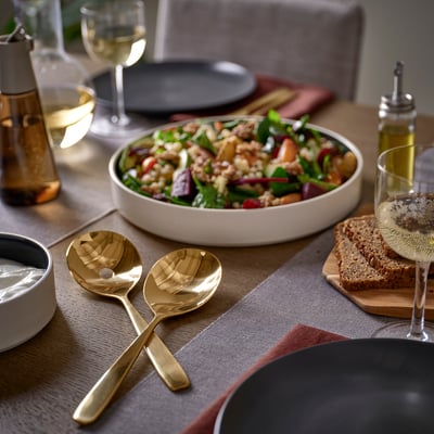 Gyllene TILLAGD skedar på bordet med salladsskål och vinglas.