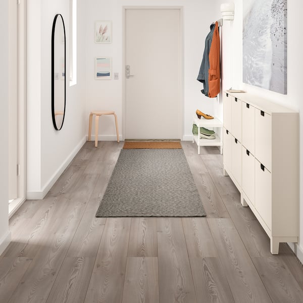 Modern hall med TIPHEDE grå matta, vit förvaring, träpall och väggkonst.