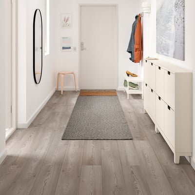 Modern hall med TIPHEDE grå matta, vit förvaring, träpall och väggkonst.