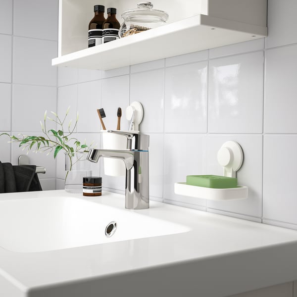 Modernt vitt handfat med kromkran. Liten TISKEN grön tvålkopp, tandborsthållare och växt. Ren, minimalistisk design.