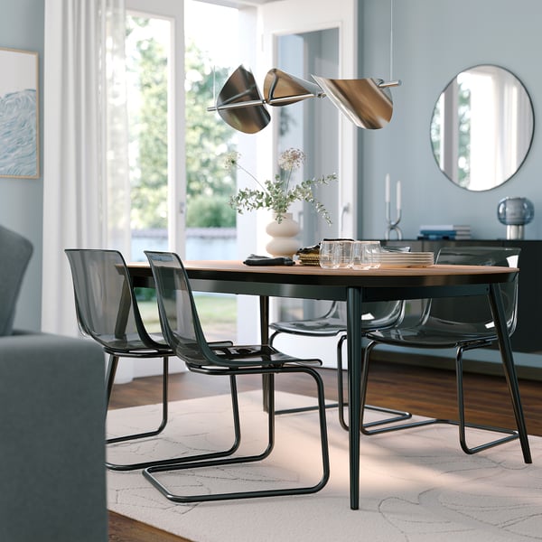 Modern matsal med rektangulärt valnötsbord, svarta metallstolar, hänglampa och spegel.