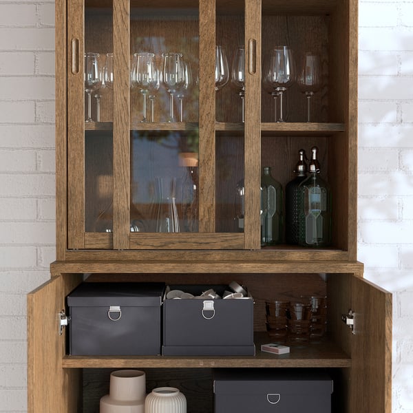 Träskåp med glasdörrar som visar vinglas och flaskor. Mjukstängande dörrar och justerbara hyllor synliga.