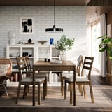 Modern matsal med ekbord, vadderade stolar, stort fönster, vit bur, grönska.