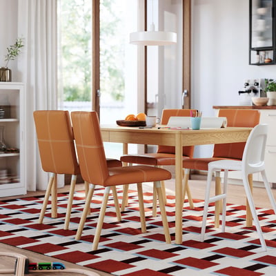 Modern matgrupp med orange läderstolar, träbord och flerfärgad matta.