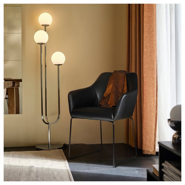 Svart modern stol med metallram, rund armatur bredvid, orange filt.