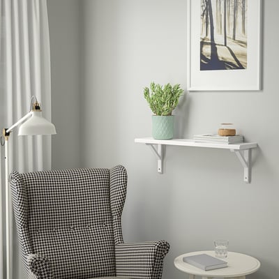 Hundtandsfåtölj, vit vägghylla med böcker och växter, blå vägg, vit gardin och skogsfoto.