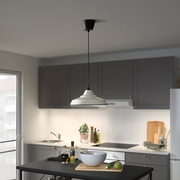 Modernt kök med mörka skåp, vita bänkar, TRETTIOEN-lampa, grönsaker på skärbräda.