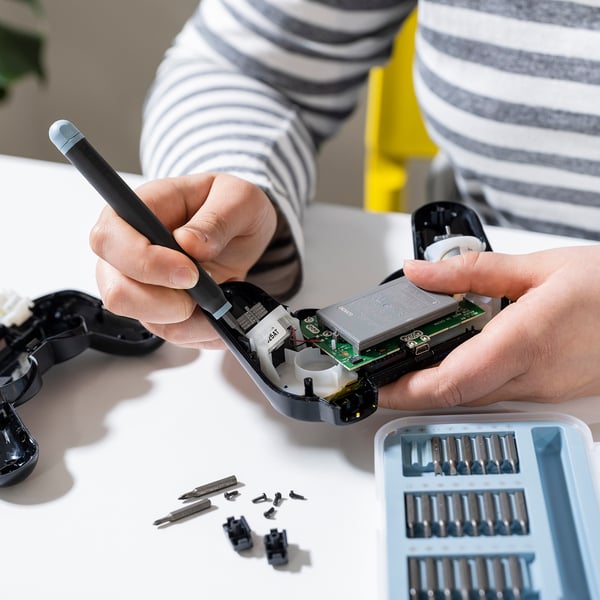 Personen reparerar en liten enhet med hjälp av TRIXIG skruvmejselsats med magnetisk bitslåda.