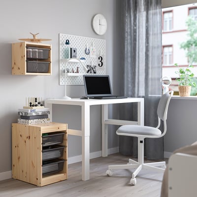 Mysigt hemmakontor med förvaring från TROFAST, vitt skrivbord, grå stol och hyllor i trä. På skrivbordet finns en bärbar dator och en anslagstavla med anteckningar och dekorationer.