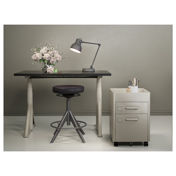 Minimalistisk arbetsplats: svart skrivbord, pall, lampa, arkivskåp, rosa blommor.