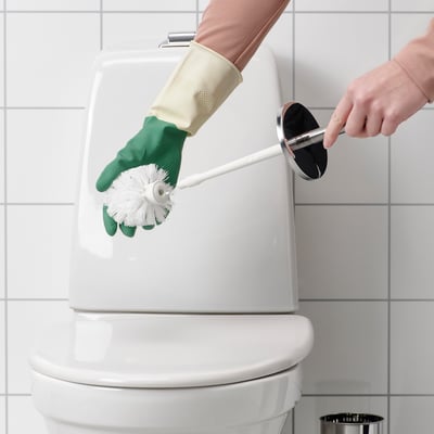 En person med handskar rengör toaletten med en borste.