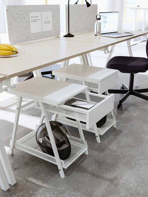 En TROTTEN förvaringsmöbel i vit metall med nätdesign, med en låsbar låda och en öppen hylla för en hjälm, perfekt för skrivbordet eller vardagsrummet.