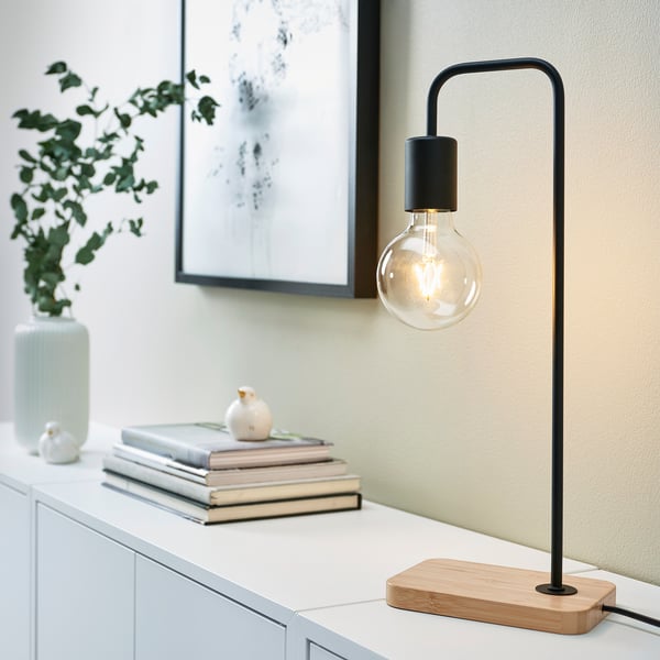 Minimalistisk svart TVÄRHAND-lampa på vit yta med dekor.