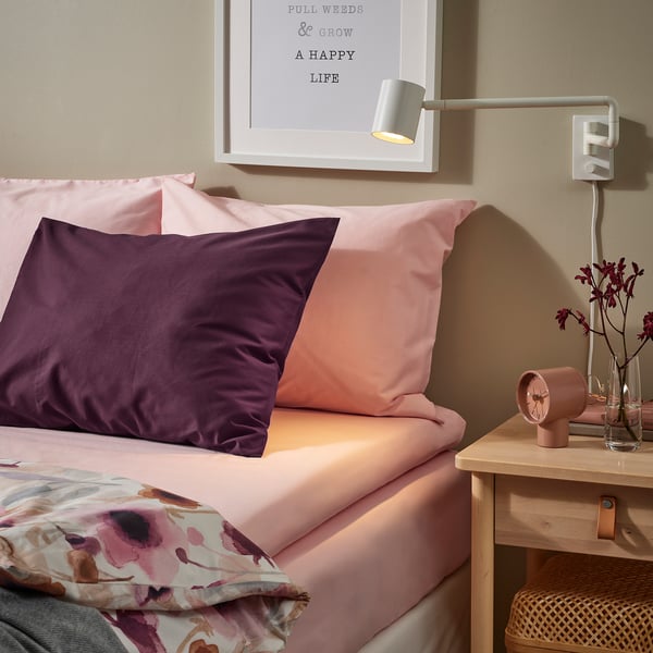 Säng med rosa ULLVIDE percale-lakan. Väggarna har abstrakt konst och väggmonterat ljus. Sängen är stor, prydnadskuddar ingår.