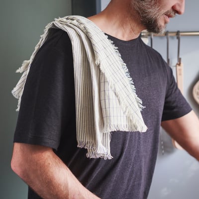 En man med en sliten, randig handduk draperad över axeln. Handduken hänger löst med fransiga ändar.