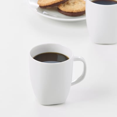 Två vita kaffekoppar bredvid en tallrik med kakor. Muggar av slitstarkt, slagtåligt fältspatporslin.