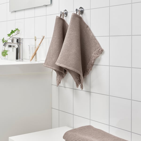 Ljusbrun VALLASÅN handduk hänger nära handfatet; mindre än tandborsthållaren.