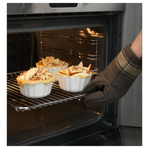 Placera minipajer för hand i en vit vågkantad form i ugnen. Bruna vantar greppskål. Rostfri ugn, pajer med äppelskivor.