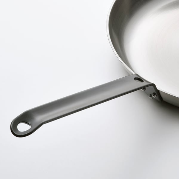 En stekpanna i rostfritt stål med ett mörkt, robust handtag som gör det säkert att lyfta.