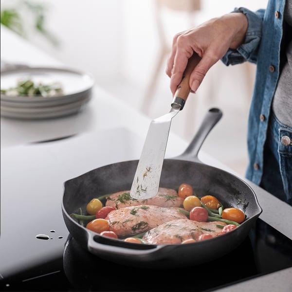 Personen vänder kokt fisk med tomater i stekpannan med hjälp av spatel.