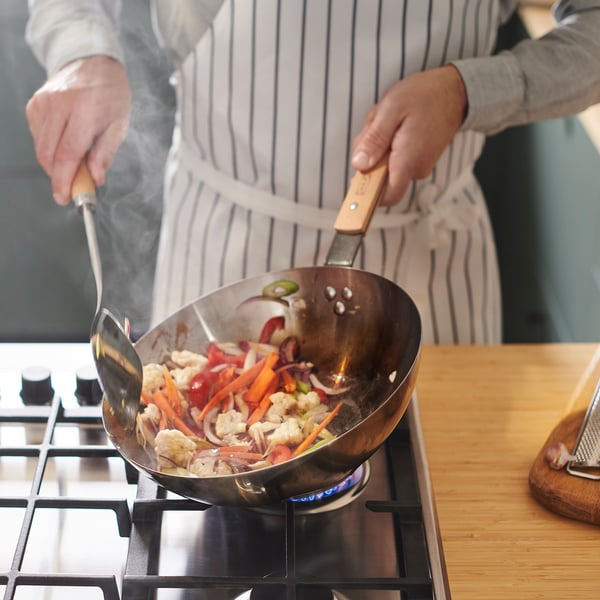 En person wokar grönsaker i en wok i kolstål på en gasspis, vilket demonstrerar dess förmåga att snabbt värma upp och till och med värmefördela.