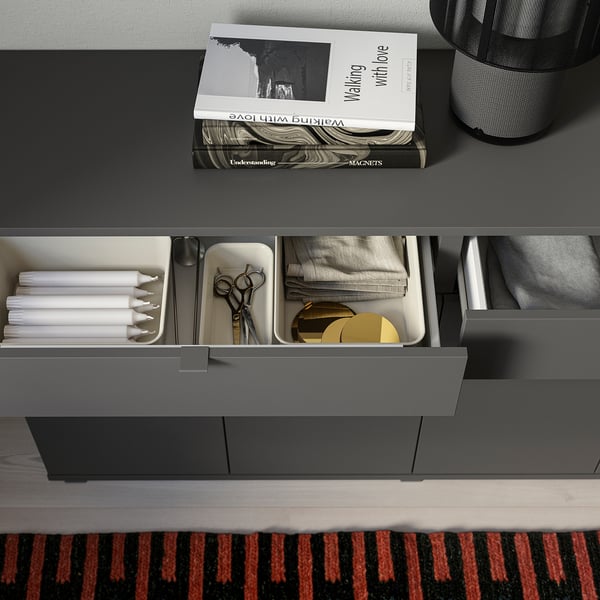 Modern grå skänk med lådor och hyllor organiserade med böcker, ljus, sax och tyg.