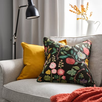 Mysigt vardagsrum med färgglad soffa, kudde VILDPERSILJA, gul kudde, svart lampa, orange blommor, röd pläd.