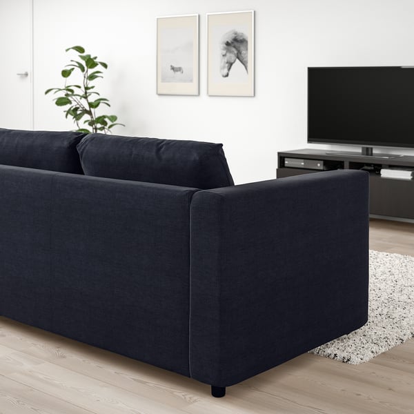 Modernt vardagsrum med VIMLE svart soffa, plattskärms-tv och konsttryck. Soffan dominerar utrymmet med elegant, mörk design.