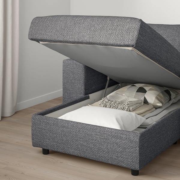 Modern stoppad soffa med öppet förvaringsfack, innehållande hopvikta filtar och kuddar.