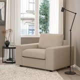 Modern beige soffstol, minimalistisk design, stor fönsterbakgrund, hög svart lampa, sidobord med torkade blommor, mysig hemmiljö.