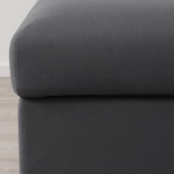 Bilden visar en närbild av en mjuk, mörkgrå soffa med slätt, slitstarkt tyg, vilket framhäver dess bekväma och högkvalitativa struktur.