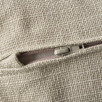 En närbild av en dragkedja på en högkvalitativ, beige texturerad soffa. Den har en robust dragkedje- och sömdetalj som framhäver dess hållbarhet och design.