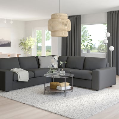 Modernt vardagsrum med VIMLE sektion, glasbord, matta och lampa. Stora fönster med gardiner.