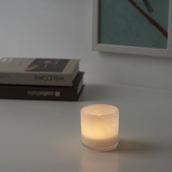 Tänd ljus i glashållare på bord, varmt sken, med böcker och inramad bild.