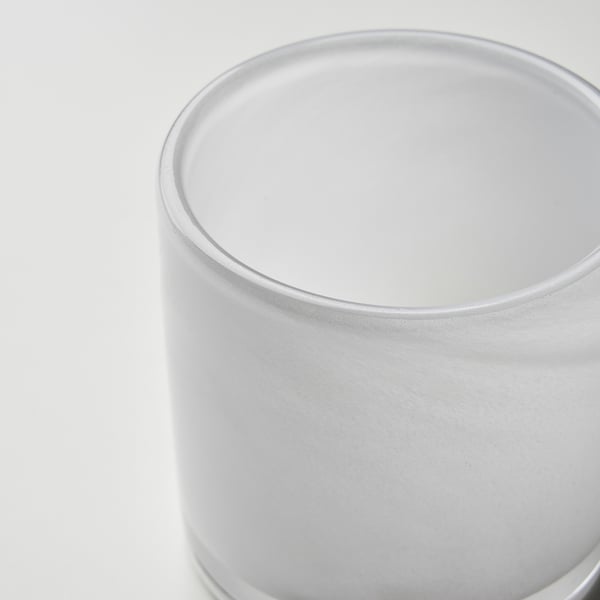 Närbild av en handgjord ljusstake i glas. Den släta, frostade ytan reflekterar ljuset subtilt.