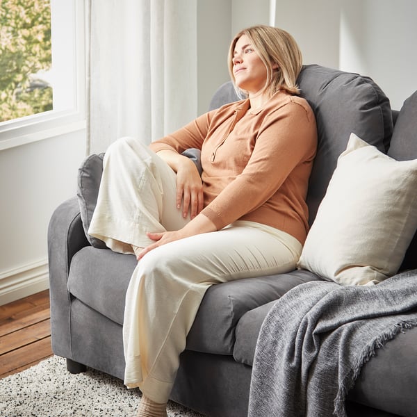 En kvinna kopplar av på en grå VINLIDEN-soffa, med en beige filt.