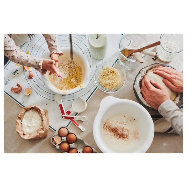 Upptagen köksscen med människor som bakar, använder blandningsskålar och olika ingredienser på en bänkskiva.