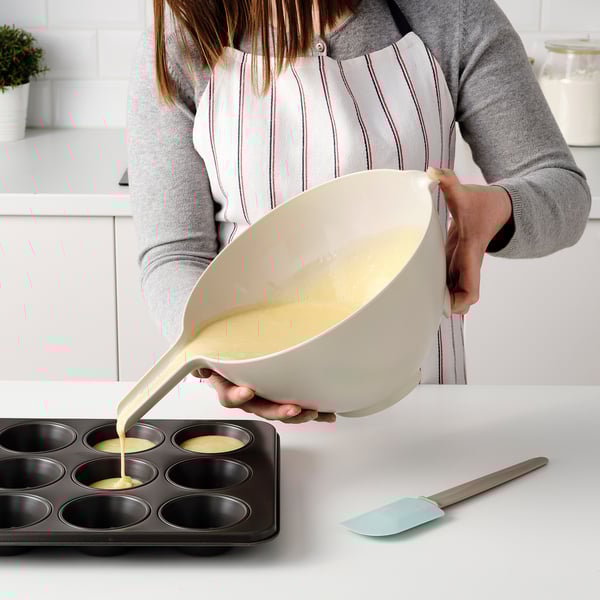 Person som häller smeten från en lutande mixerskål i en muffinsform.