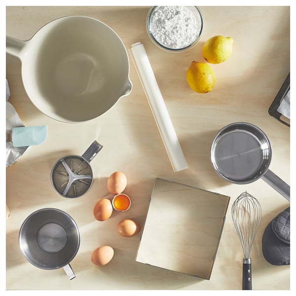 En vit VISPNING-blandningsskål och olika bakingredienser och verktyg på en träyta.
