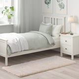 Sovrum med vit säng, plyschmatta VOLLERSLEV, gröna sängkläder, växt och lampa.