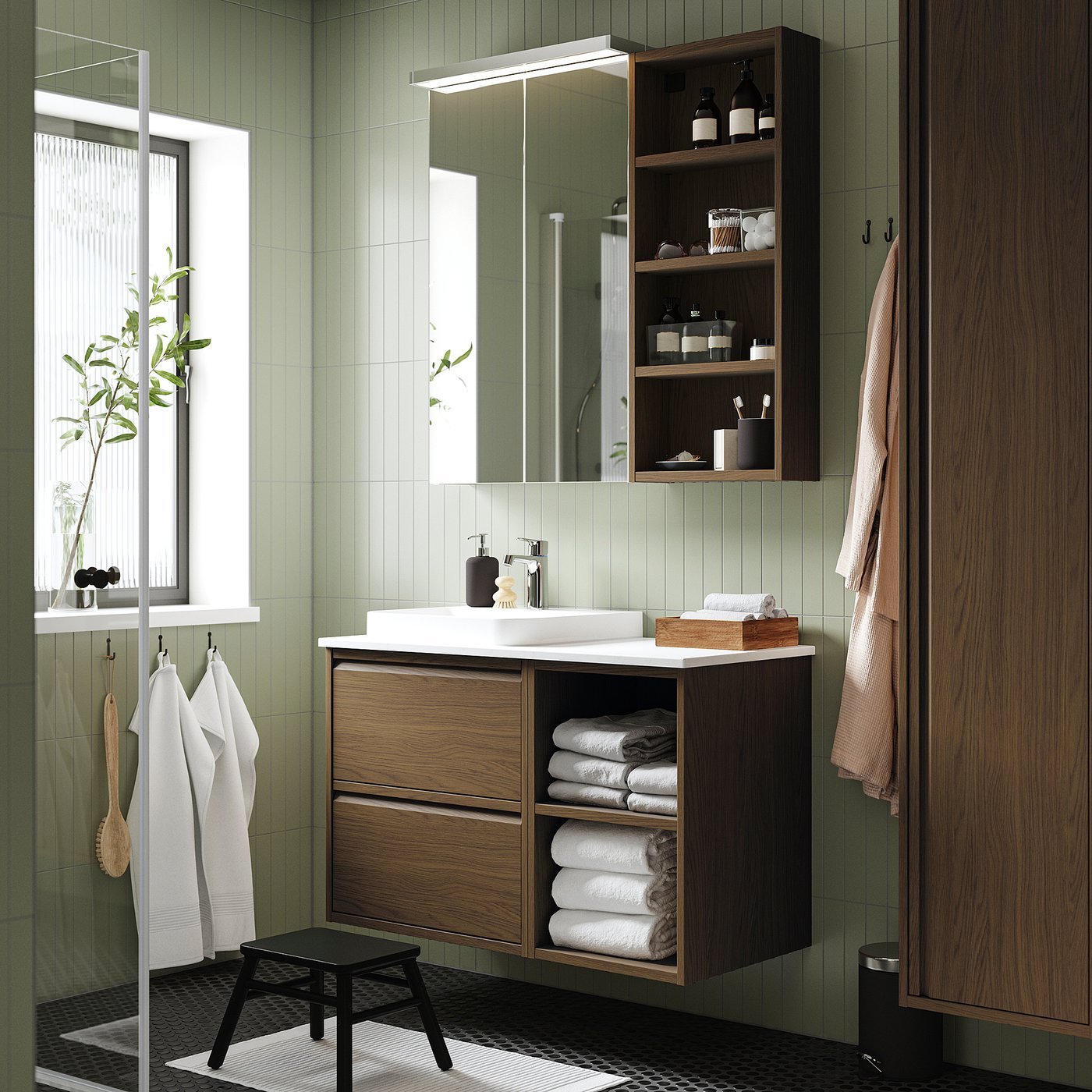 Salle de bain verte avec meuble-lavabo ÄNGSJÖN en bois foncé, lavabo blanc, miroir et rangement.