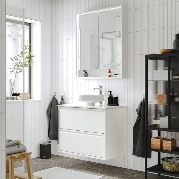 Salle de bains blanche moderne avec meuble-lavabo élégant ÄNGSJÖN, lavabo rond, serviettes grises et accents noirs.