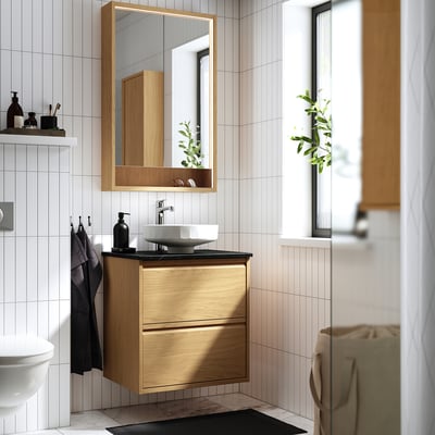 Salle de bain moderne avec meuble-lavabo ÄNGSJÖN, lavabo rond, miroir. Minimaliste, murs blancs, accents noirs, serviettes, plantes.